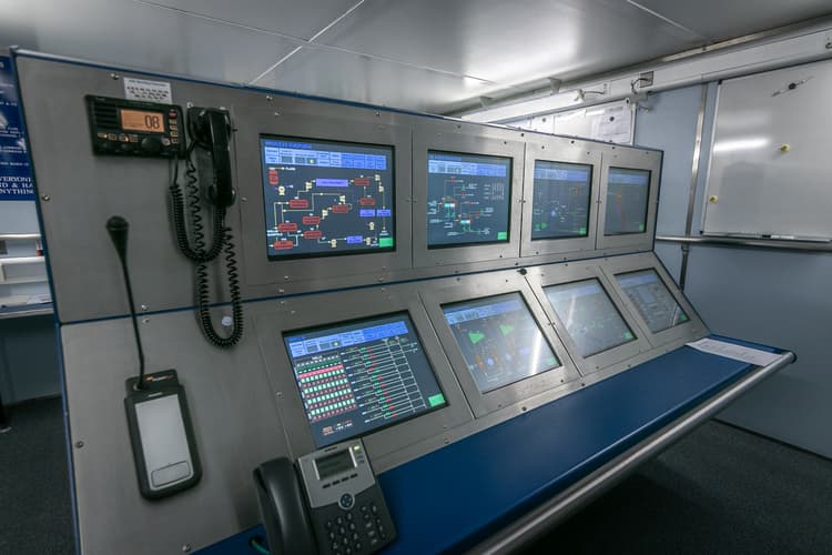 a control room panel with multiple digital screens displaying complex system diagrams, flowcharts, and monitoring data.