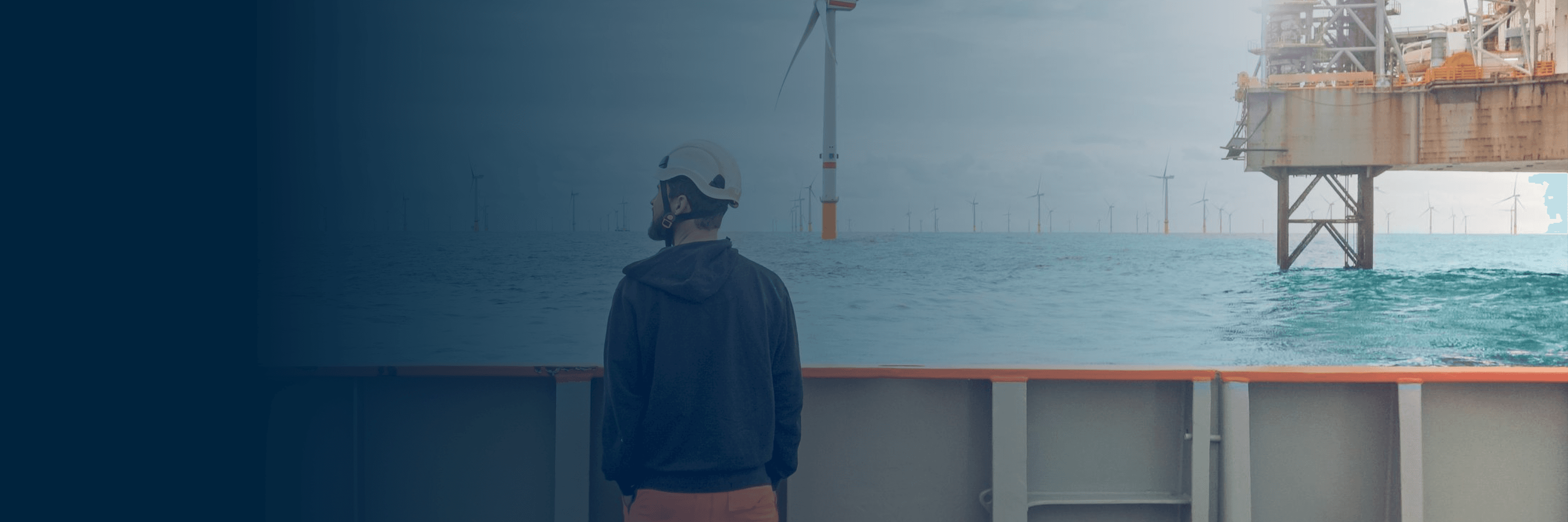 Offshore worker on a rig looking at wind turbines and oil and gas platform.