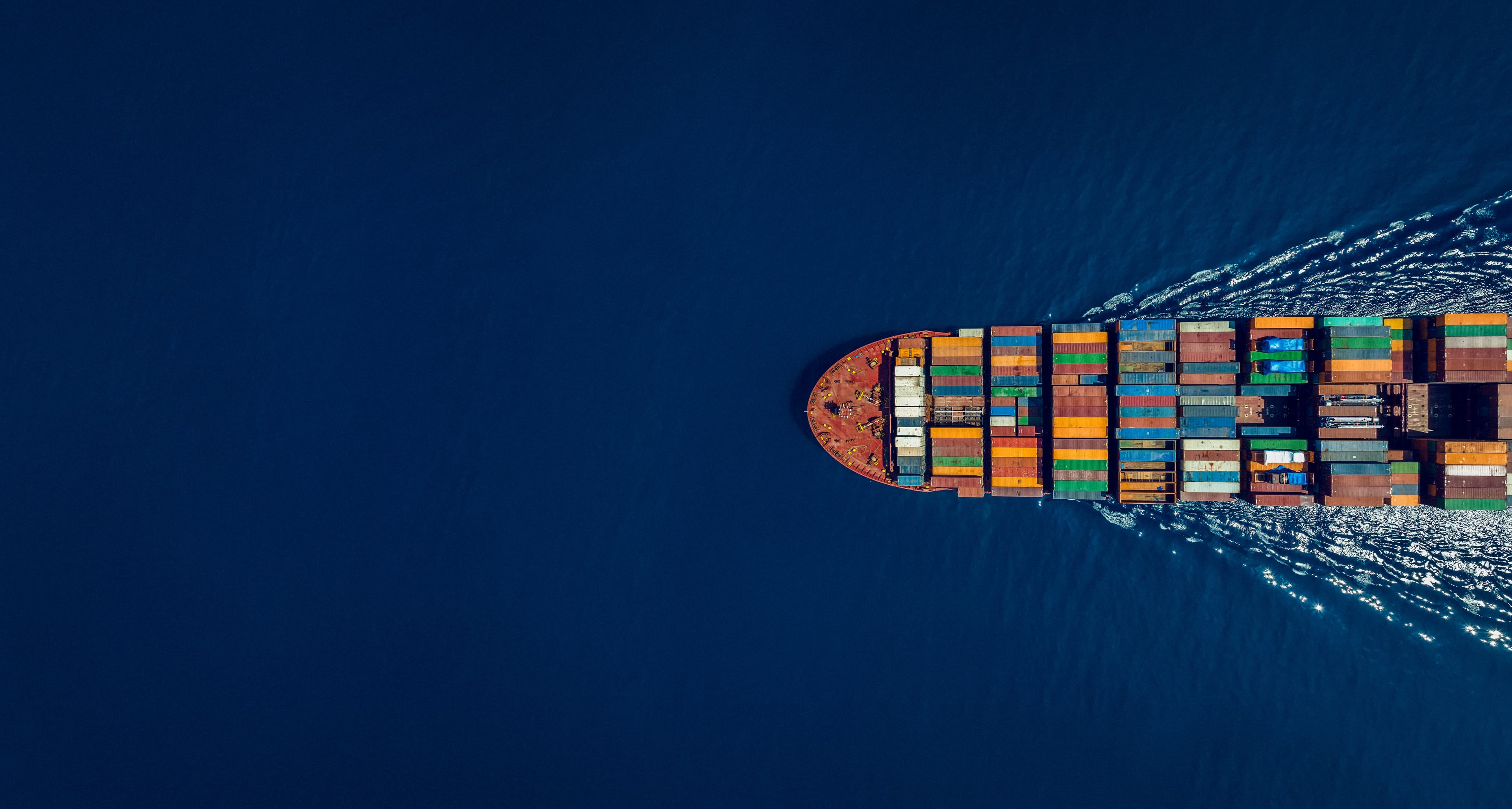 An aerial view of a container ship sailing through open waters, carrying multicoloured containers, symbolising global trade, logistics, and maritime transport efficiency.