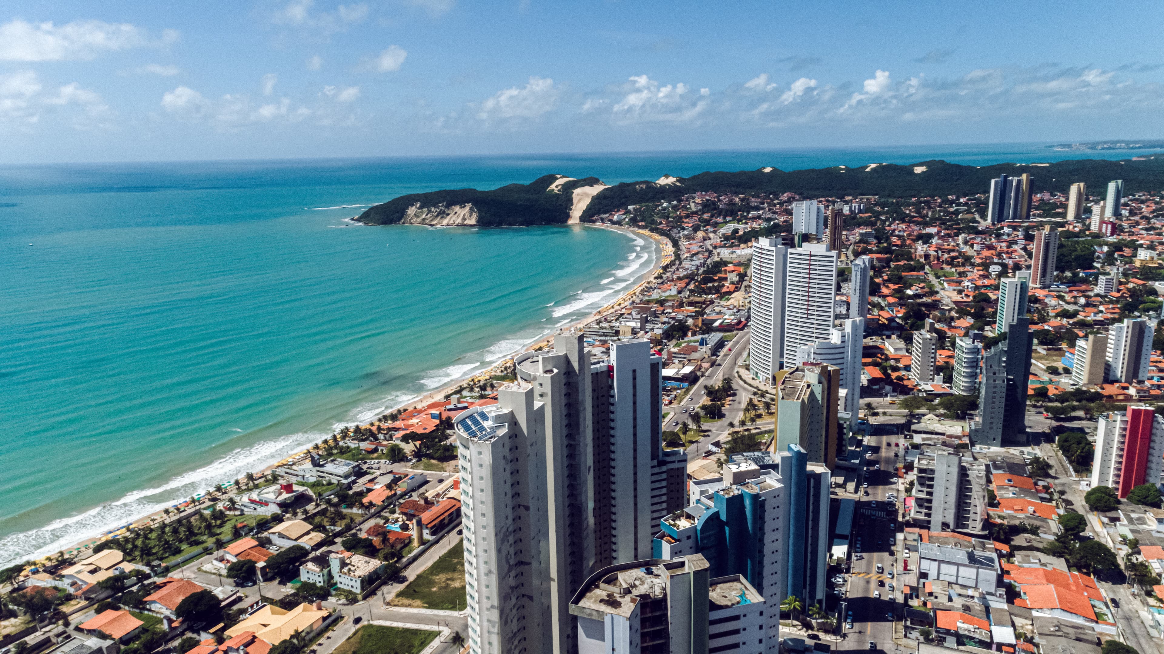 A scenic aerial view of Natal, Rio Grande do Norte, with its stunning beaches, high-rise buildings, and famous Morro do Careca sand dune, offering a blend of natural beauty and urban appeal.