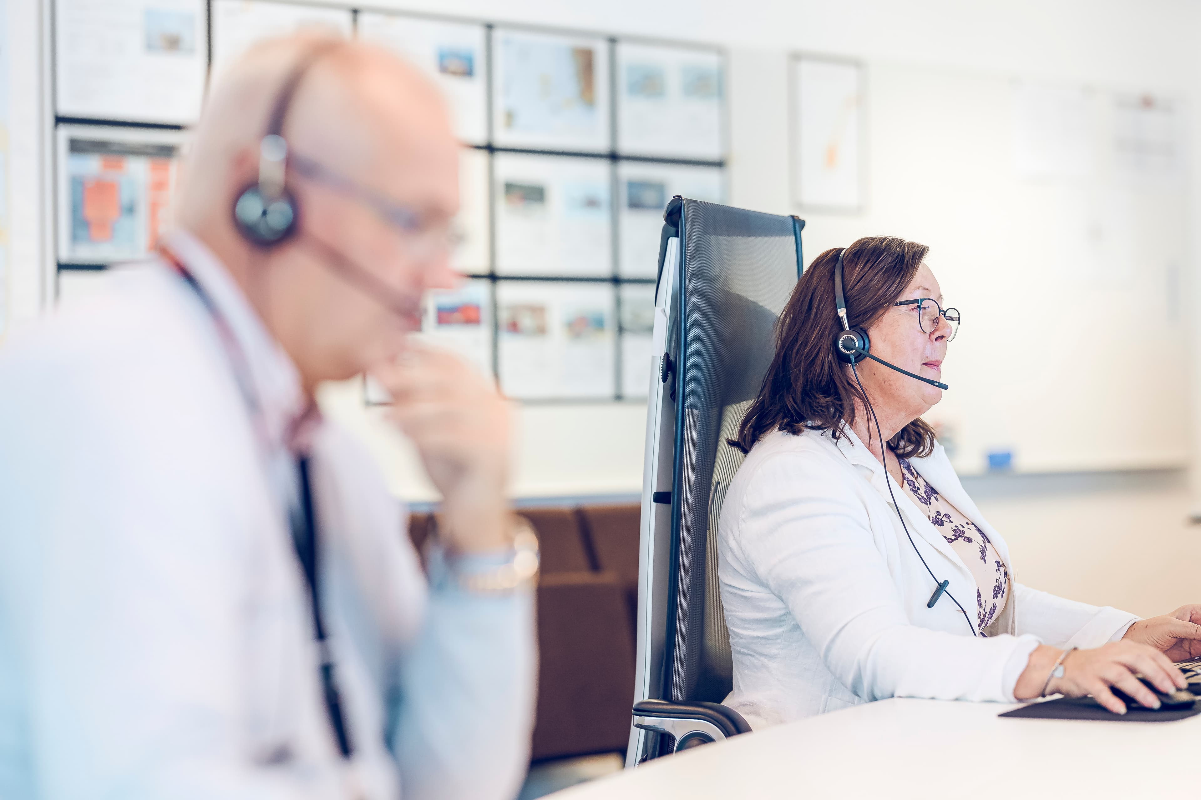two professionals wearing headsets, working attentively at desks in an office setting. T